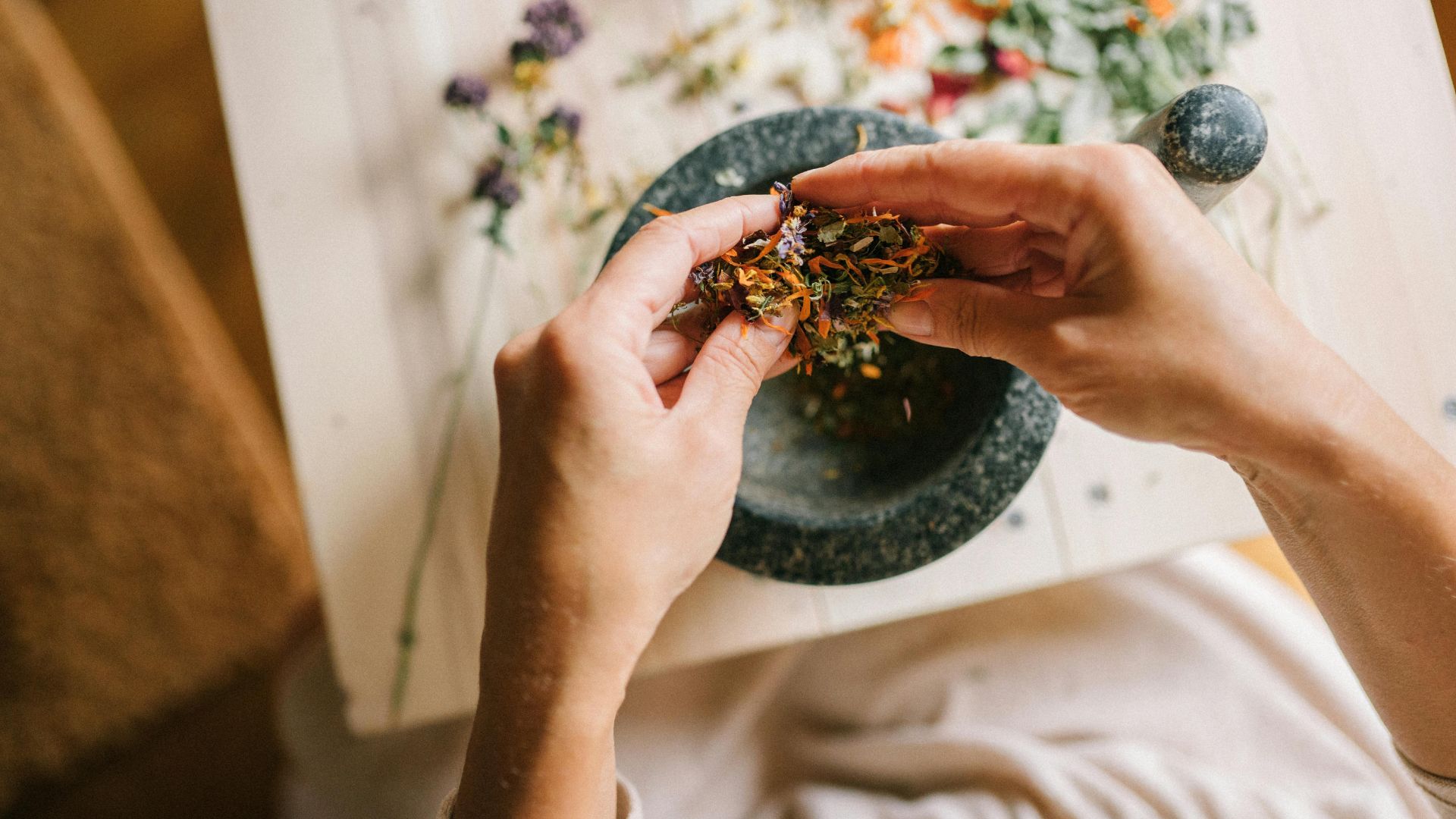 Hands preparing dried herbs in a stone mortar with floral background