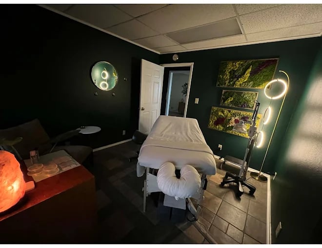 Dimly lit massage room with massage table, salt lamp, and nature artwork